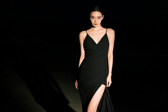 Elegant woman in black dress with thigh-high slit.